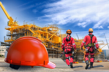 Orange hard safety helmet on floor two worker safety man wear equipment PPE and safety harness in the site of rig construction background