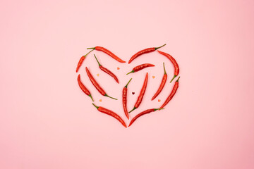 Red hot chilli peppers in the form of the heart lie on a pink background table