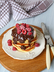 fresh homemade pancakes with berries and chocolate, sprinkled with powdered sugar on a white wooden background. Ukrainian and Russian national cuisine