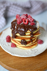 fresh homemade pancakes with berries and chocolate, sprinkled with powdered sugar on a white wooden background. Ukrainian and Russian national cuisine