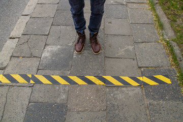 Male feet in boots on the sidewalk in front of a black and yellow stripe..