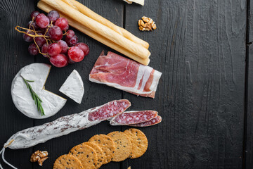 Assortment of cheese and meat appetizers, on black wooden table, top view  with copy space for text