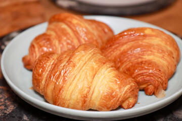 A plate of three freshly made croissants on a plate in a kitchen on a wooden work top