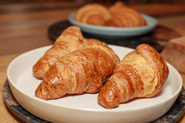 A plate of three freshly made croissants on a plate in a kitchen on a wooden work top