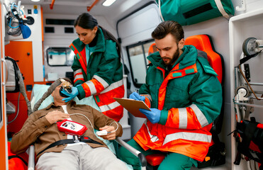 A paramedic woman in uniform puts on a ventilator with oxygen to help a senior patient lying with a...