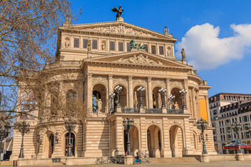 Fototapeta na wymiar Square in the center of the city of Frankfurt. Buildings of the historic old opera house with trees and commercial buildings at springtime in sunshine. Bicycles in front of the steps