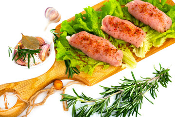 Pieces of meat lie on a cutting board with herbs and rosemary. Semi-finished meat products