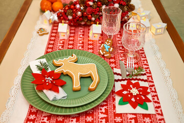 Christmas table setting with tree, garlands, poinsettia, wineglass ,gingerbread cookies and lights on a table covered with a red and white tablecloth