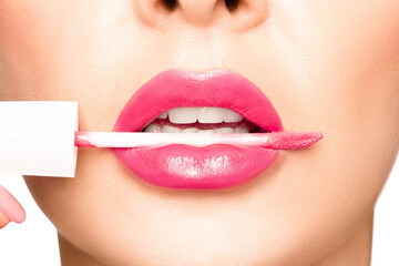 Naklejka premium Girl lips with pink lipstick. In the mouth, an applicator for applying lipstick..
