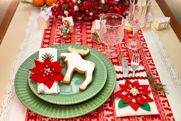 Christmas table setting with tree, garlands, poinsettia, wineglass ,gingerbread cookies and lights on a table covered with a red and white tablecloth