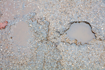 Mit Wasser gefülltes Schlagloch auf einer nassen Straße.