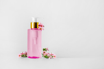 Pink bottle with hydrophilic oil on a light background. Pink flowers nearby..