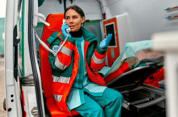 Beautiful woman paramedic in uniform answers the phone call while sitting in a modern ambulance car.