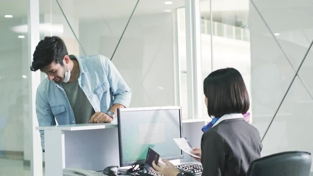 Travelers give passport to female officer at airline check in counter for issue airplane ticket boarding pass. Passengers wearing mask.Flight attendant create the air ticket. Place the pink baggage. 
