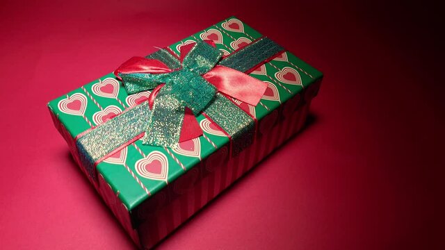 gift box with ribbons and hearts on a red background in a beam of light, congratulations and surprise for Valentine's Day, Christmas or wedding