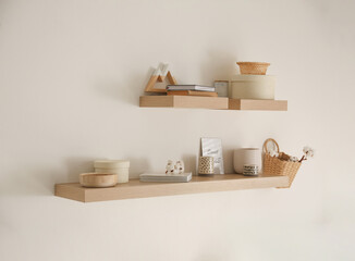 Wooden shelves with books and different decorative elements on light wall