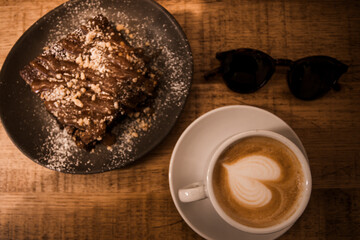 Plate with slice of tasty homemade chocolate cake on wooden table. Homemade brownie cake with a fresh tasty italian cappuccino for an healthy breakfast.