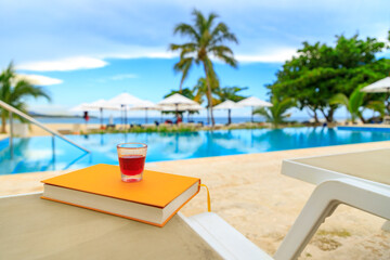 Red liquor on a yellow book by the pool. Holiday mood, recreation, relaxation.