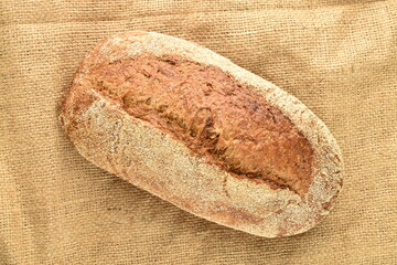 One loaf of freshly baked buckwheat bread, close-up, on a jute fabric.