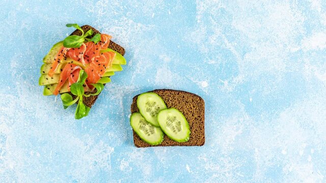 Stop motion animation of healthy snack or appetizer toast with salmon, avocado, shrimps,  eggs, cucumber, lambs lettuce or corn salad and parsley. Step by step preparation of food, top view video