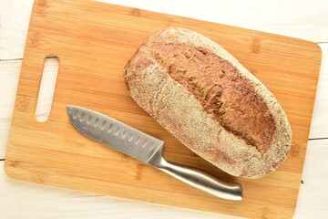 One loaf of freshly baked buckwheat bread with a metal knife, close-up, on a bamboo board.