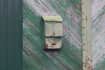 one old green metal mailbox hanging on a  wooden fence in the street