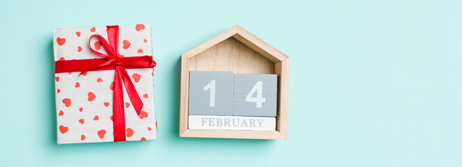 Top view of white gift boxes with hearts and wooden calendar on colorful background. The fourteenth of February. Valentine's Day concept