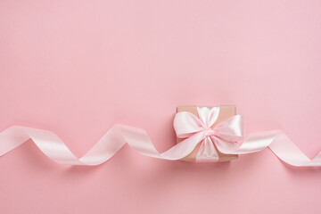Gift box with long ribbon on pastel pink background. Present for Valentines Day, Mother's Day or Women's Day. Festive monochrome background. Top view flat lay with free space.