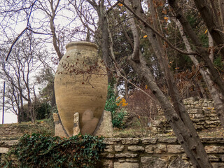 Big ceramic pot in the autumn botanical garden. Plants with autumn leaves around.