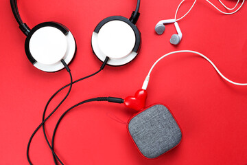 A heart-shaped headphone splitter for a couple in love. Connected to a red portable speaker and two pairs of headphones - flat lay. Valentine's day, love, modern technology, copy space