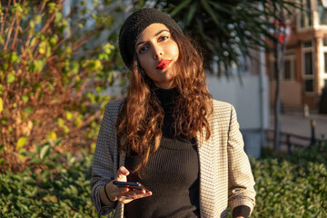 Portrait of a gorgeous stylish Persian girl holding a phone on the street during sunset 