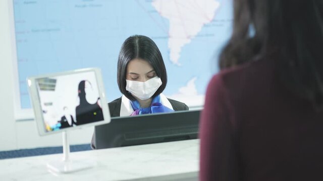 Travelers give passport to female officer at airline check in counter for issue airplane ticket boarding pass. Passengers wearing mask.Flight attendant create the air ticket. Place the pink baggage. 