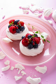 Pavlova meringue cake with cream and berries on dusted sugar pink background