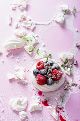 Pavlova meringue cake with cream and berries on dusted sugar pink background