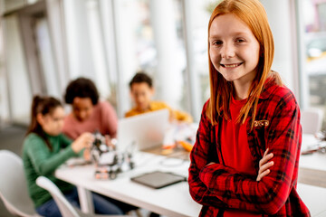 Cute little girl standing in front of kids programming electric toys and robots at robotics classroom