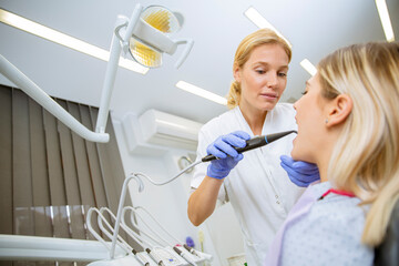Female doctor in uniform checking up female patient's teeth in dental clinic