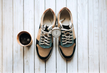 Modern suede new sneakers stand on a wooden white background with a stopwatch and a cup of coffee. Sport, movement, copy space. A pair of trend shoes, concept, walk, lunch, respite.