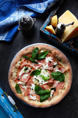 Pizza with ham. Traditional Italian pizza. Metal plate for serving pizza. A piece of parmesan. Blue cotton napkin. Vertical photo. The view from the top.