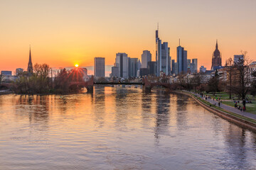 Fototapeta na wymiar Sunset over the Frankfurt skyline. Skyscrapers, commercial buildings on the horizon. River Main with bridge and park on the bank. Reflections of the sun in the water