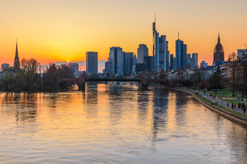 Fototapeta na wymiar Frankfurt skyline in the evening at sunset. River with reflections in the water of the skyscraper. Financial and business district in the center of the city. Park near the shore with trees