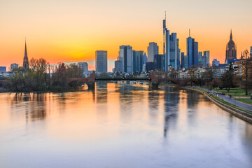 Fototapeta na wymiar Sunset over the Frankfurt skyline in spring. Skyscrapers and skyscrapers from the financial and business hub of the city. River Main with reflections and bridge with park