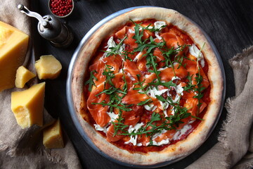 Pizza with red river fish. Traditional Italian pizza. Metal plate for serving. A piece of parmesan and red peppercorns. View from above.