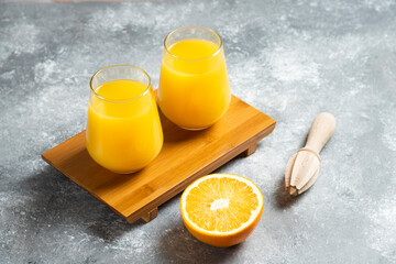 Glass cups of orange juice and a wooden reamer