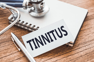 TINNITUS - text on card on wooden table with stethoscope and notepad for medical records.