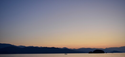 Fototapeta premium Silhouette of a fishing boat and the dark blue mountains in the background
