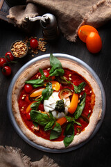 Pizza with burrata cheese and pine nuts. Italian pizza. Metal plate for serving. Green basil leaves. Vertical photo. View from above.