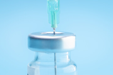 Punctured syringe in a bottle to put a vaccine on blue background.