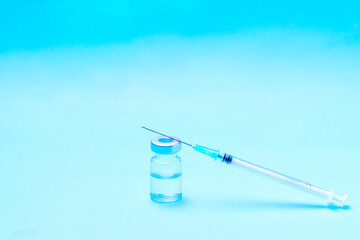 Syringe on top of a bottle to put a vaccine on a blue background.