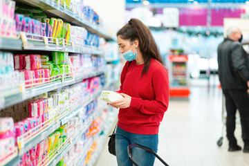 A young woman in a mask chooses a product in a store. The concept of consumerism and shopping during the coronavirus pandemic