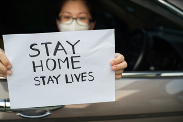 Women wearing a face mask showing Stay Home Sign while sitting in car